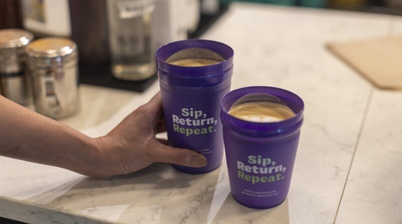 Two purple cups full of coffee. A hand holds one. Both read,